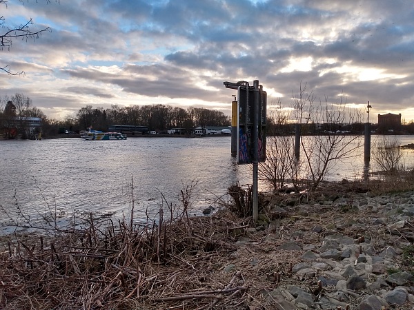 Das Bild zeigt ein Schild und hohen Wasserstand der Weser nach einer Sturmflut entlang des Bremer Osterdeichs. 